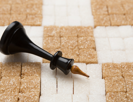 Black King lying on chessboard made of brown and white lump sugar, copy spaceの写真素材