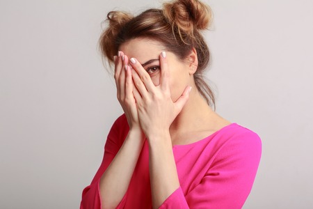 Joyful woman hiding face, having fun on grey backgroundの写真素材