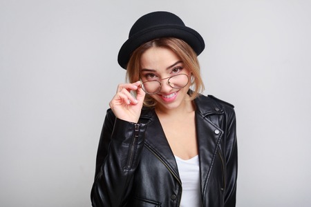 Joyful woman posing with glasses in black jacket over grey studio background