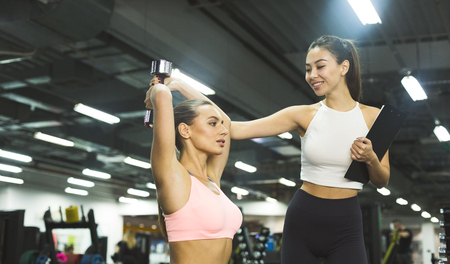 Personal coach helping girl doing exercises with dumbbells in sport centerの写真素材