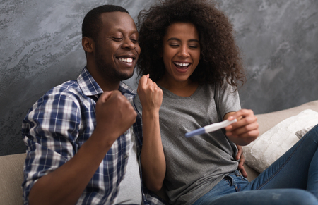 Happy afro-american couple looking pregnancy test with yes-gesture. Happy future parents conceptの写真素材