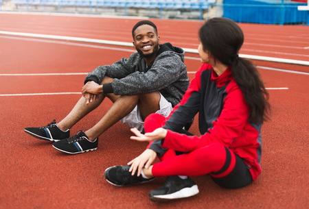 Sporty couple wearing sport clothes relaxing after training, sitting at sports ground. Fitness together conceptの写真素材