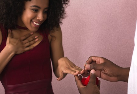 Man making proposal to his happy surprised girlfriend putting engagement ring on her fingerの写真素材