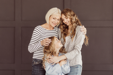 Granny, mother and daughter enjoying time together, posing against brown wall at homeの写真素材