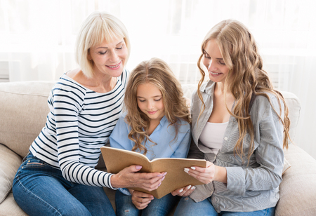 Happy family watching photo album, sitting on sofa at homeの写真素材
