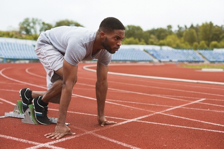 Fit afro-american sportsman on starting position, ready to run at the stadiumの写真素材