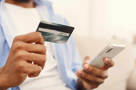 Online payment. African-american man making transaction using mobile application on his smartphone and credit card, closeupの写真素材