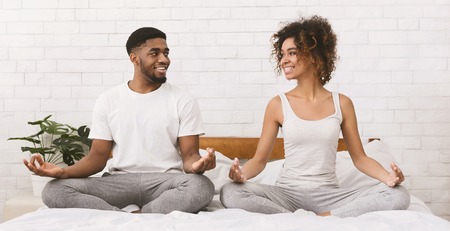 Tantric connection. African-american couple meditating in lotus position on bed, panoramaの写真素材