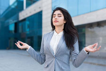 Beautiful young business woman doing meditation on the office building background. Recharge yourself conceptの写真素材