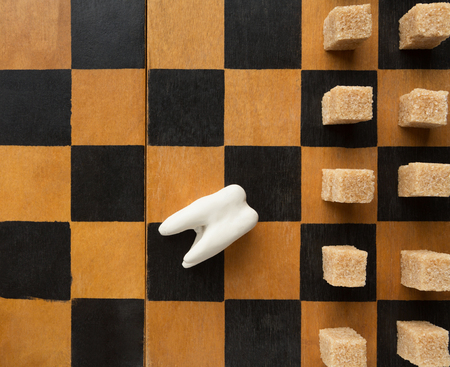Lost in fight with sweets. Broken white teeth lying on chessboard, loser to cane sugar cubes, top viewの写真素材