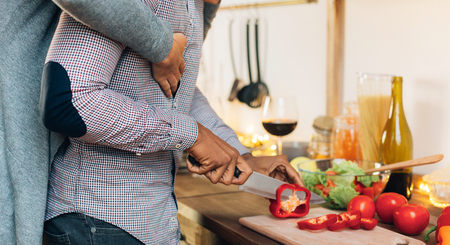 Amorous african-american couple cooking together in kitchen, woman embracing her cooking boyfriend,...
