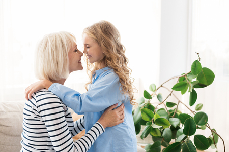 Little girl and her grandmother spending time together, hugging at homeの写真素材