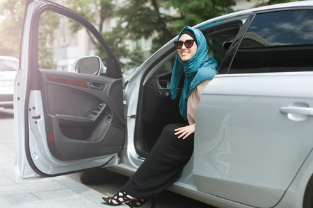 Smiling arabian lady in sunglasses sitting in her car with open car door.の写真素材