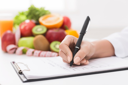 Doctor writing prescription for patient, making diet plan at workplace with fresh fruits, panoramaの写真素材