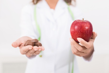 Food diet option dilemma. Woman nutritionist offering fresh apple as alternative to unhealthy milk chocolate,copy spaceの写真素材