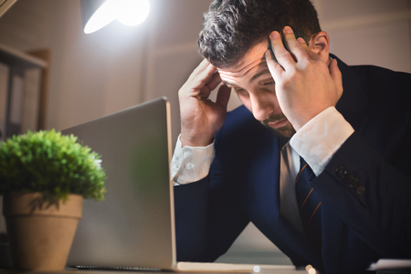 Tired male worker with headache, looking at laptop and thinking about deadlineの写真素材