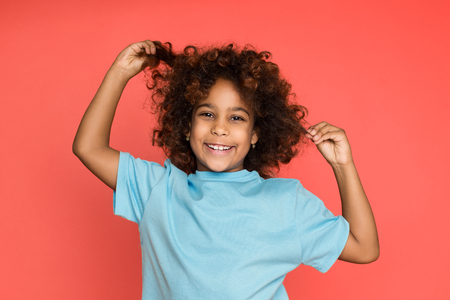 Happy little girl playing with her hair, looking at camera over pinkの写真素材