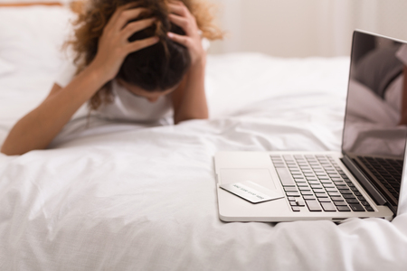 Online shopping. Credit card on laptop with worry woman on the bedの写真素材