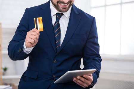 Businessman doing online purchases with credit card and tablet in office, cropの写真素材