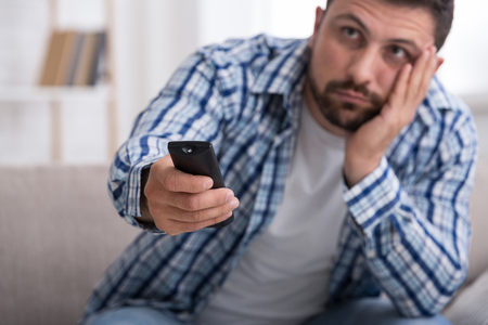 Nothing interesting to watch. Bored man with remote control watching TV at home