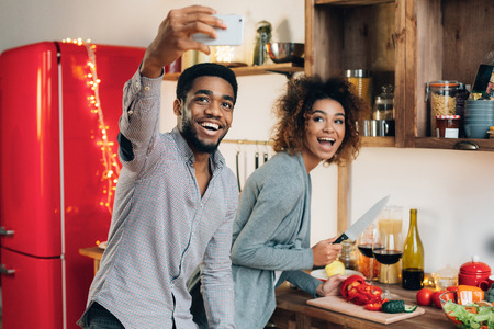 Happy couple in kitchen making selfie on smartphone, preparing dinner. Millennials lifestyle conceptの写真素材