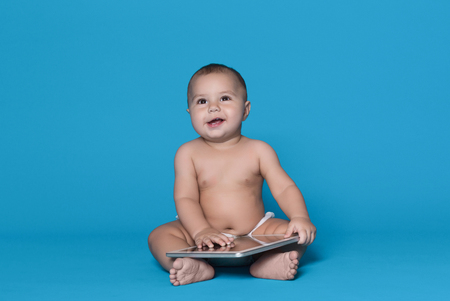 Baby and digital world. Interested little boy using digital tablet, using interactive application, sitting on blue studio backgroundの写真素材