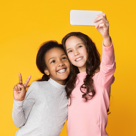Best friends taking selfie on smartphone, having fun on shine yellow backgroundの写真素材