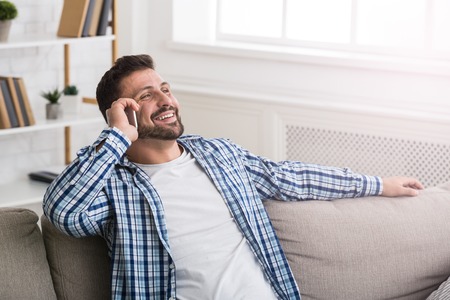 Handsome man talking on mobile phone and smiling, sitting on couchの写真素材