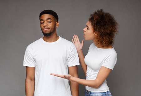 Relationship problems. Young black woman arguing with her boyfriend that ignoring her, gray studio backgroundの写真素材