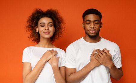 Grateful african-american couple keep both palms on chest with closed eyes, express gratitude and...