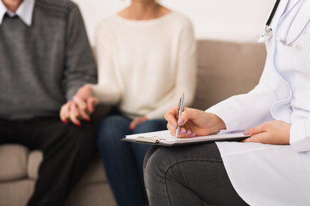 Doctor writing medical report of senior couple, visiting them at homeの写真素材