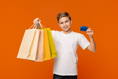 Cheerful boy showing his shopping bags and credit or debit card, orange backgroundの写真素材