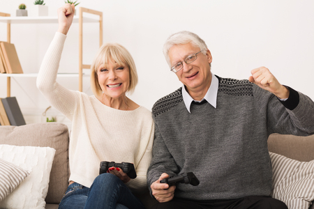 Elderly couple playing video games, celebrating victory together, having fun at homeの写真素材