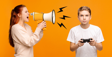 Ignore real communication. Young angry woman shouting loudly through megaphone at boy with joystick, orange panorama backgroundの写真素材