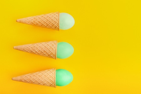 Green Easter eggs in waffle cones on yellow background. Bright creative backdrop, top view, copy spaceの写真素材