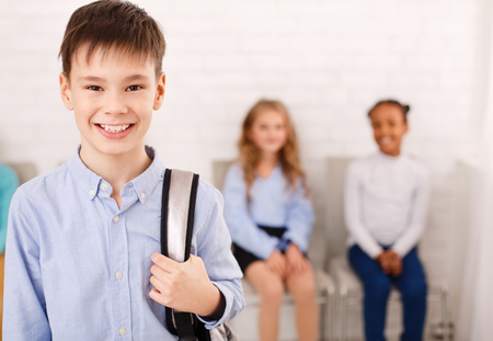 Back to school concept. Happy boy with backpack, standing at his classmates backgroundの写真素材