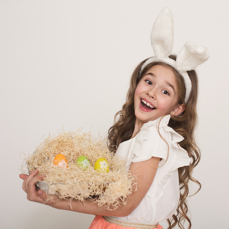 Adorable Easter bunny. Cute happy little girl with rabbit ears holding bright colorful eggs in...