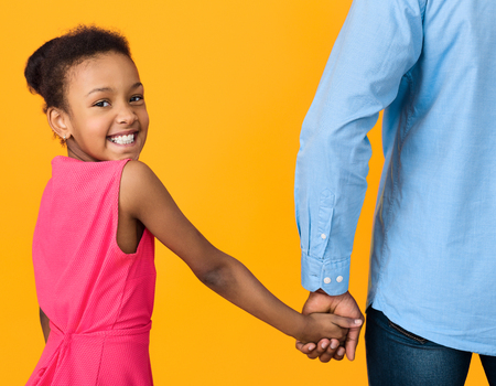 African-american girl holding fathers hand and looking at camera on yellow backgroundの写真素材