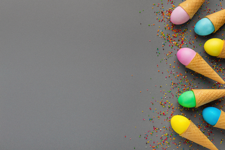 Easter greeting card. Colorful eggs in waffle cones and sprinkles on gray background, top view, copy spaceの写真素材