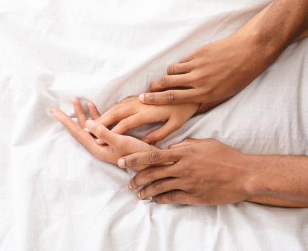 Make love. African-american male and female hands on bed, closeupの写真素材