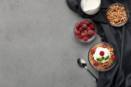 Granola with yogurt in bowls, raspberries and milk on grey background, top view, copy space....