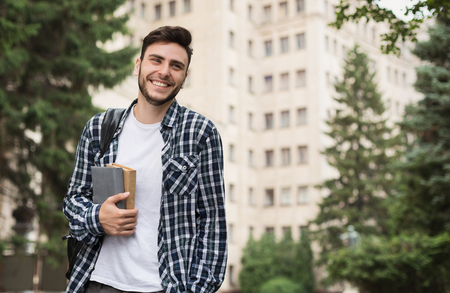 Happy male student holding books near universityの写真素材