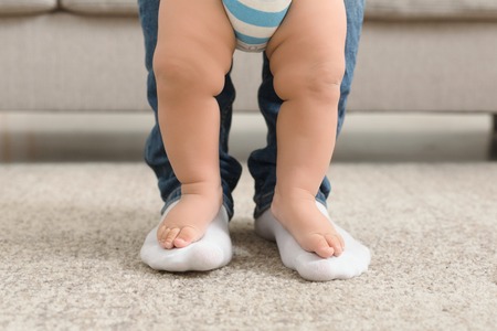 First step. Cute little baby feet standing on big daddy ones, parental support in learning to walkの写真素材