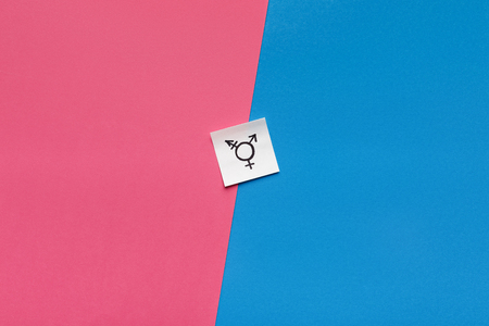 Choosing between genders. Sex selection. Paper card with transgender symbol on pink and blue backgroundの写真素材