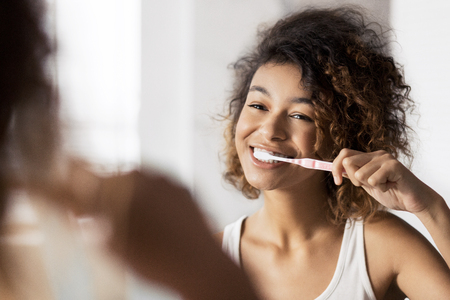 Smiling young afro woman with toothbrush cleaning teeth at bathroom. Dental care conceptの写真素材