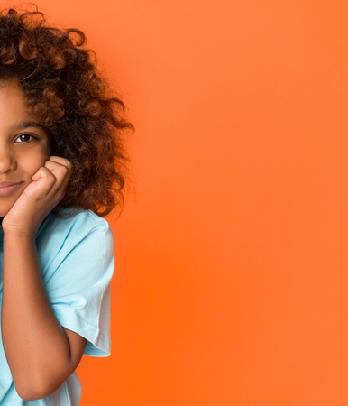 Half face portrait of schoolgirl with dark curly hair over orange backgroundの写真素材