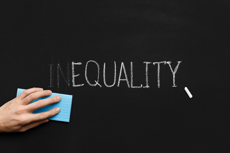 Equality concept. Male hand cleaning part In in word Inequality on chalkboard backgroundの写真素材