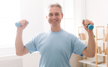 Mature man doing fitness training with dumbbells at homeの写真素材