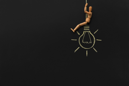Creative thinking concept. Wooden mannequin sitting on drawn electric bulb and thinking about new ideas, chalkboard background with free spaceの写真素材