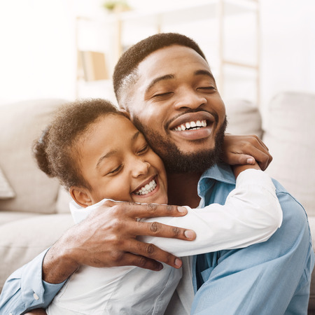 African-american daughter hugging father with love and tenderness at home, cropの写真素材